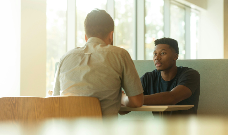 Discussion Deux personnes sont assises face à face à une table dans une pièce chaleureusement éclairée.