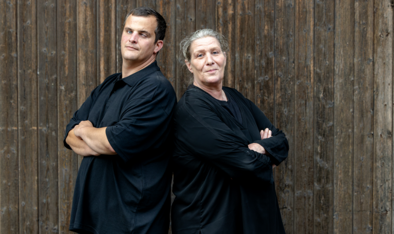 Diego c. und Carole M. Ein Mann und eine Frau stehen mit dem Rücken aneinander, halten die Arme verschränkt und blicken in die Kamera.